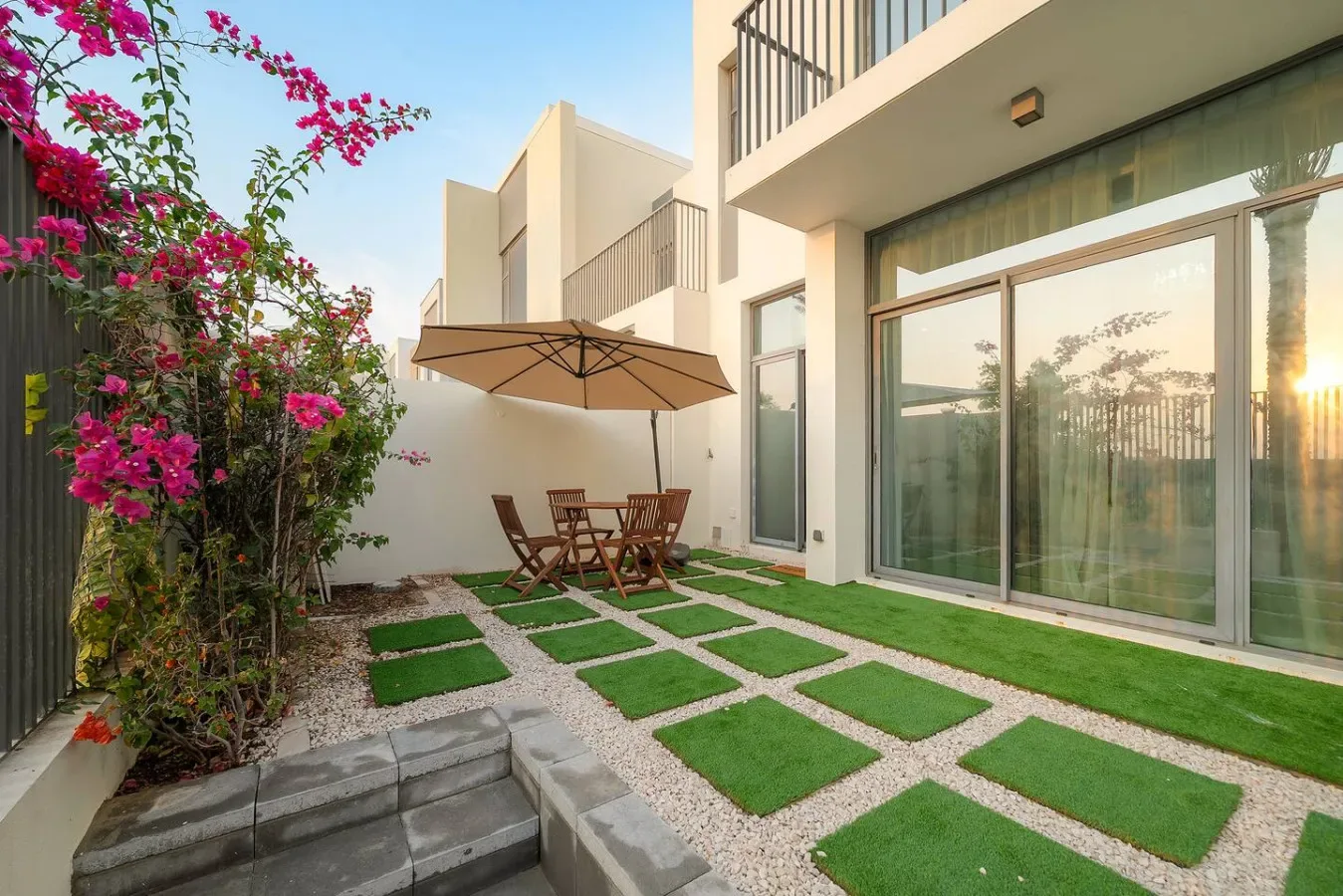 Un patio moderno tiene una mesa bajo una sombrilla y puertas corredizas de vidrio.