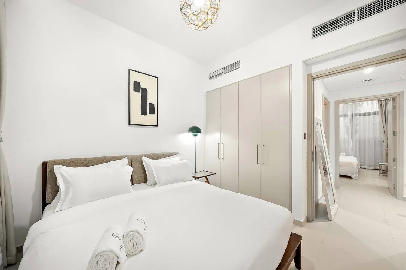 Un dormitorio luminoso con una cama bien hecha y armarios claros.