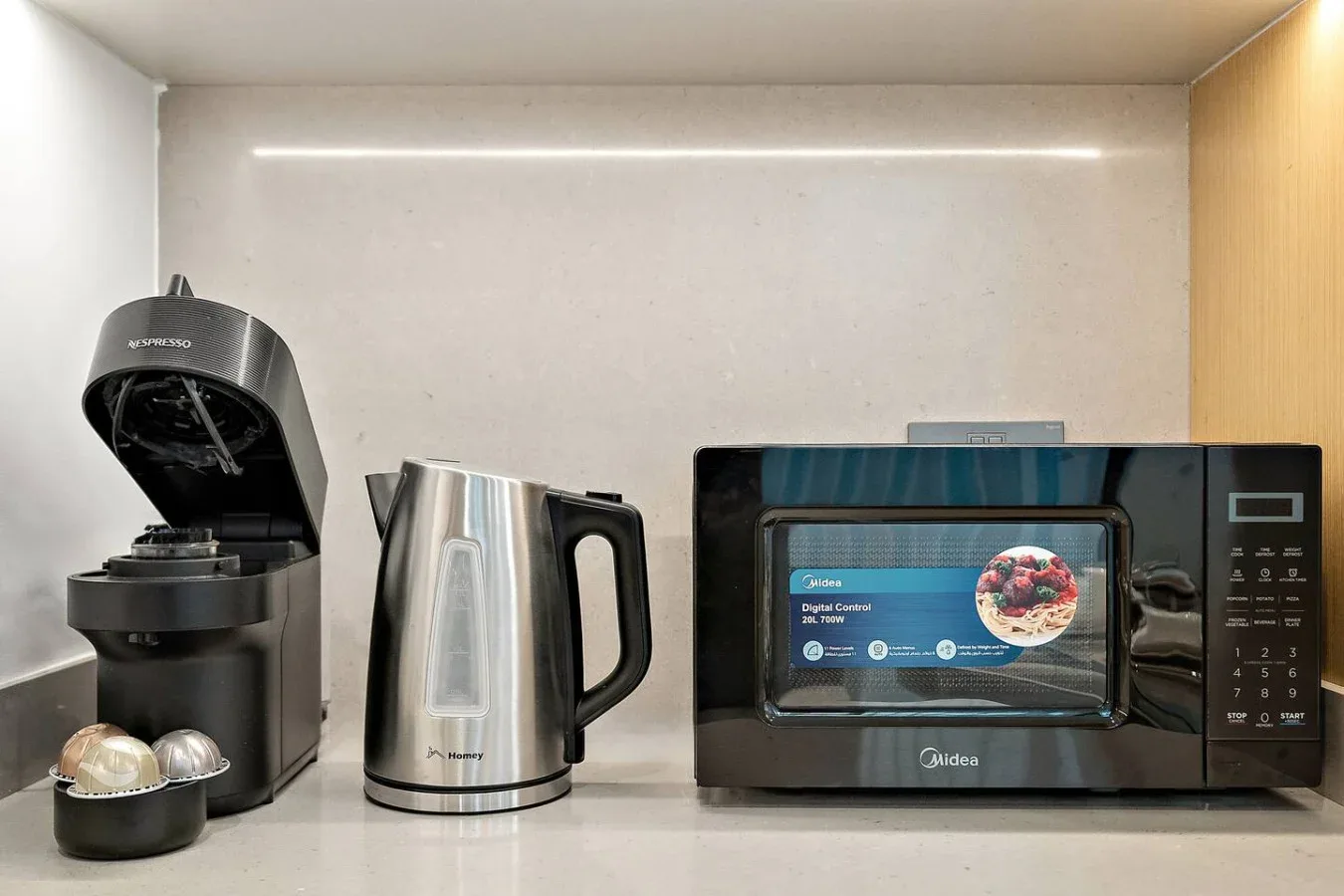 Una encimera de cocina con cafetera, hervidor eléctrico y microondas.
