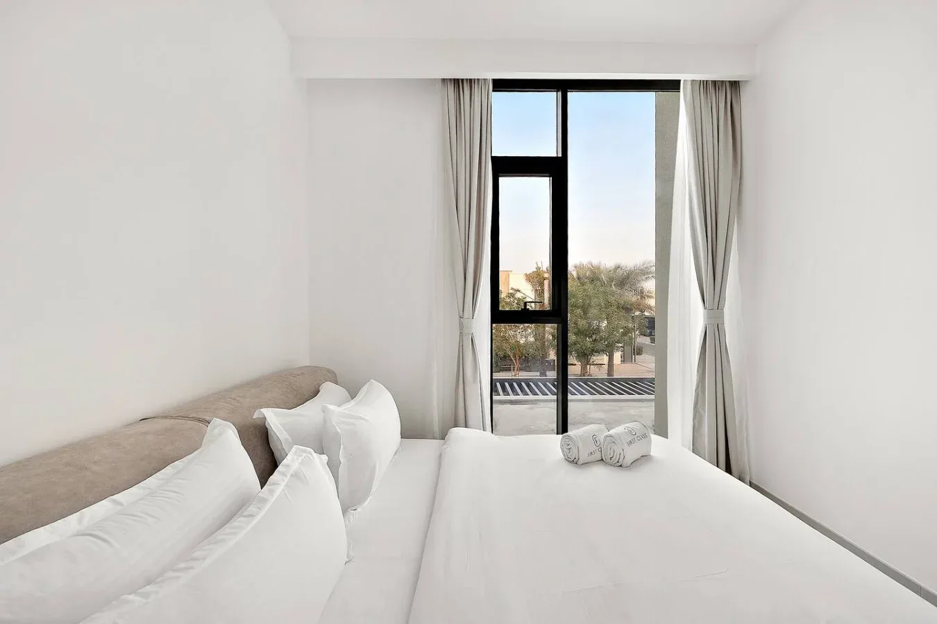 Un dormitorio luminoso con una cama blanca junto a una ventana amplia.
