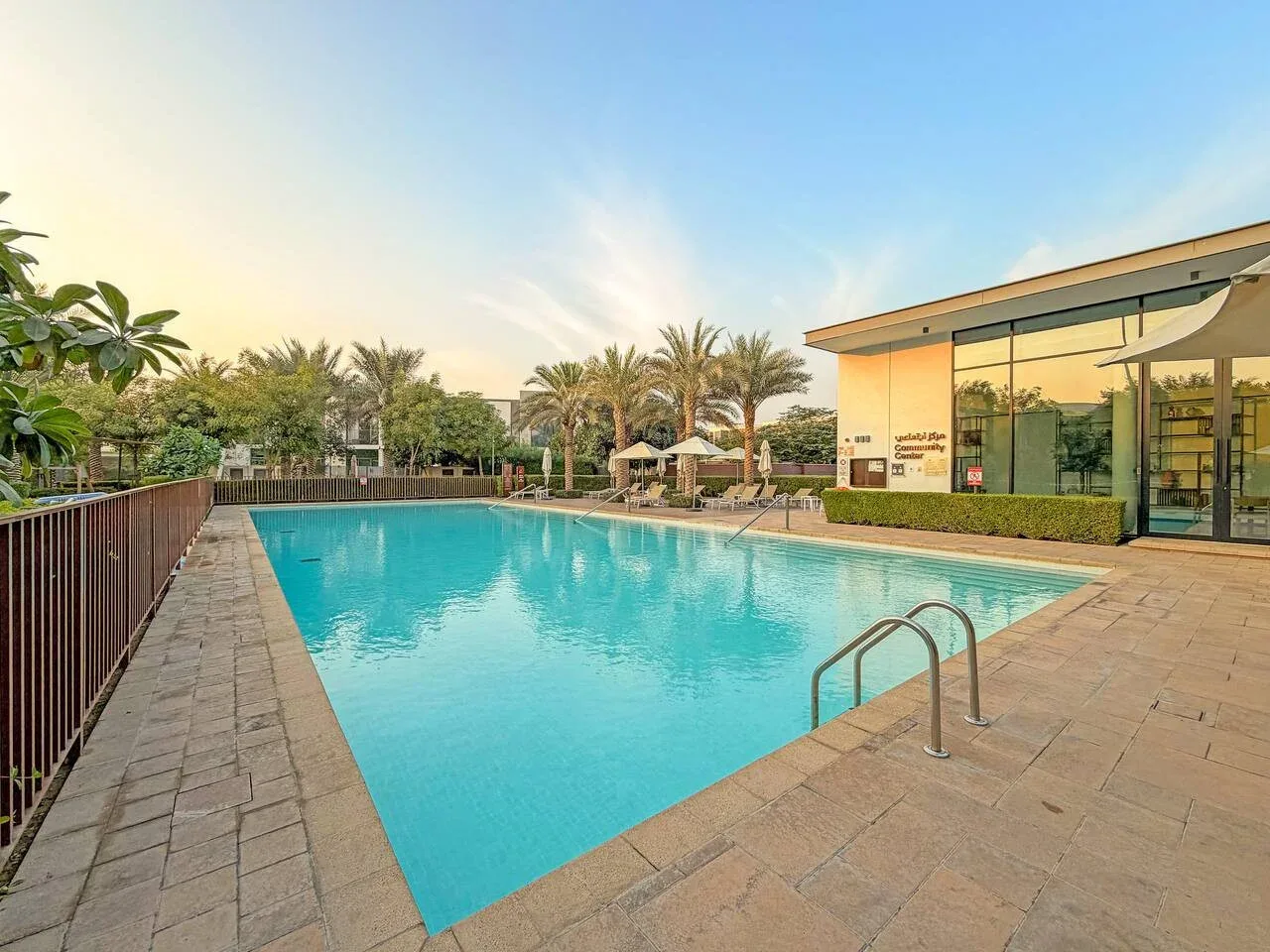 Una piscina al aire libre junto a un edificio con fachada de vidrio y palmeras.