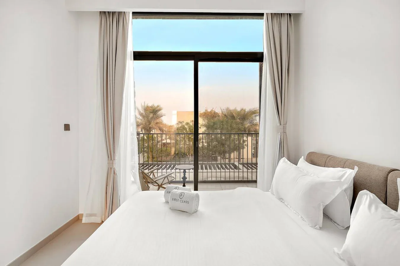 Un dormitorio luminoso con una cama blanca junto a una ventana grande que da a un balcón.