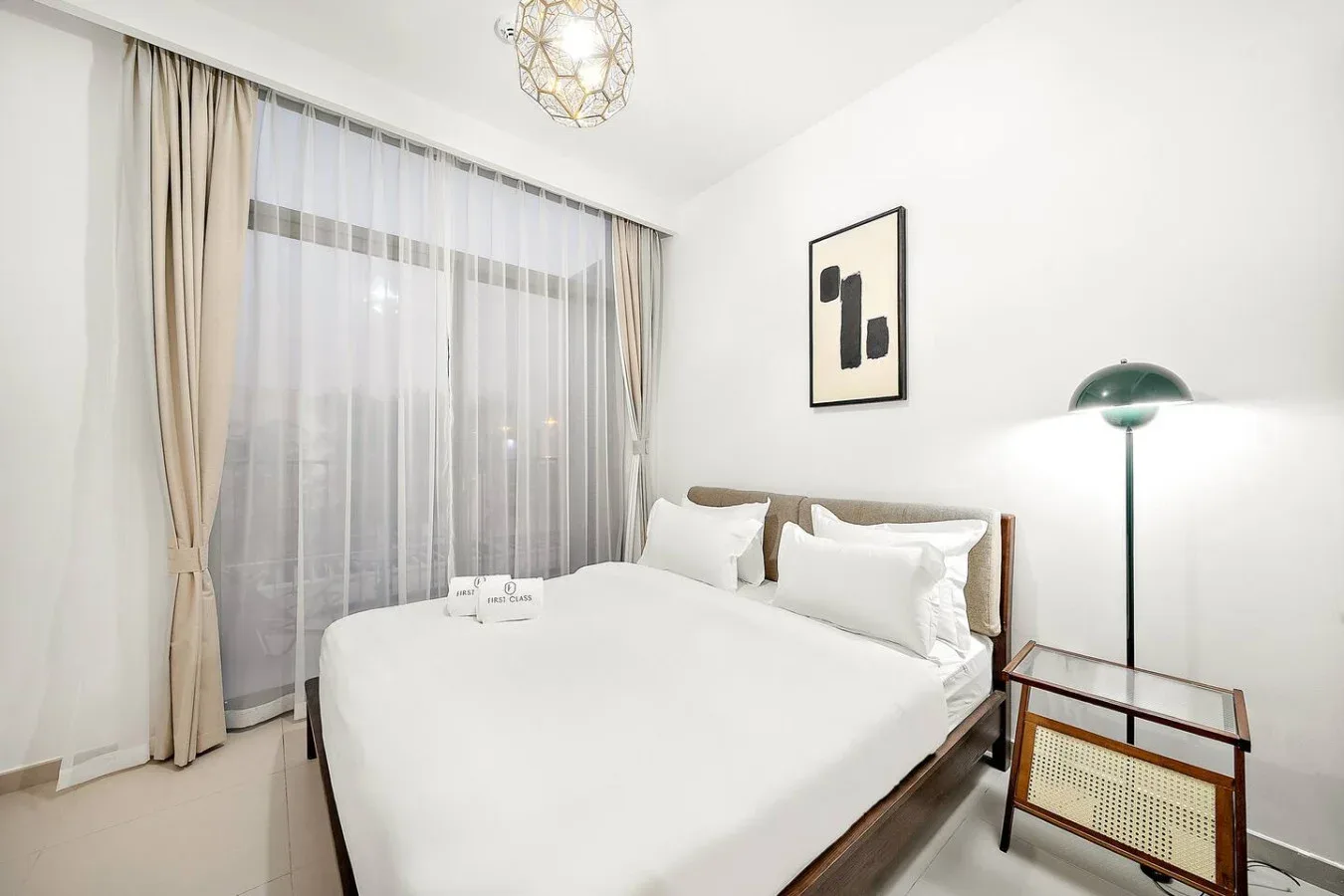 Un dormitorio con una cama bien tendida junto a una gran ventana con cortinas.
