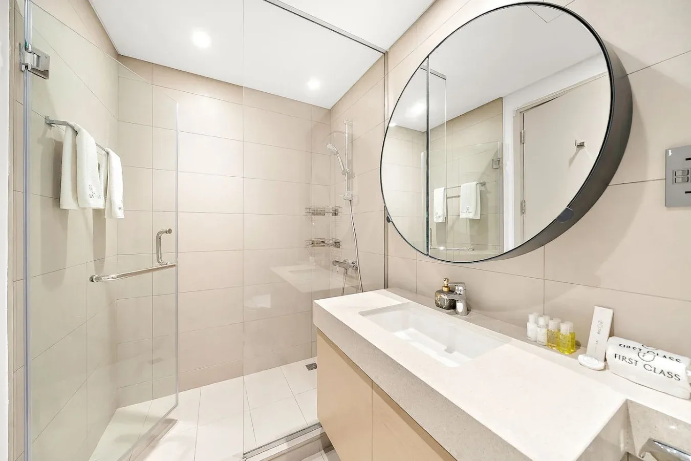 Un baño luminoso con un lavabo alargado y un espejo redondo grande.