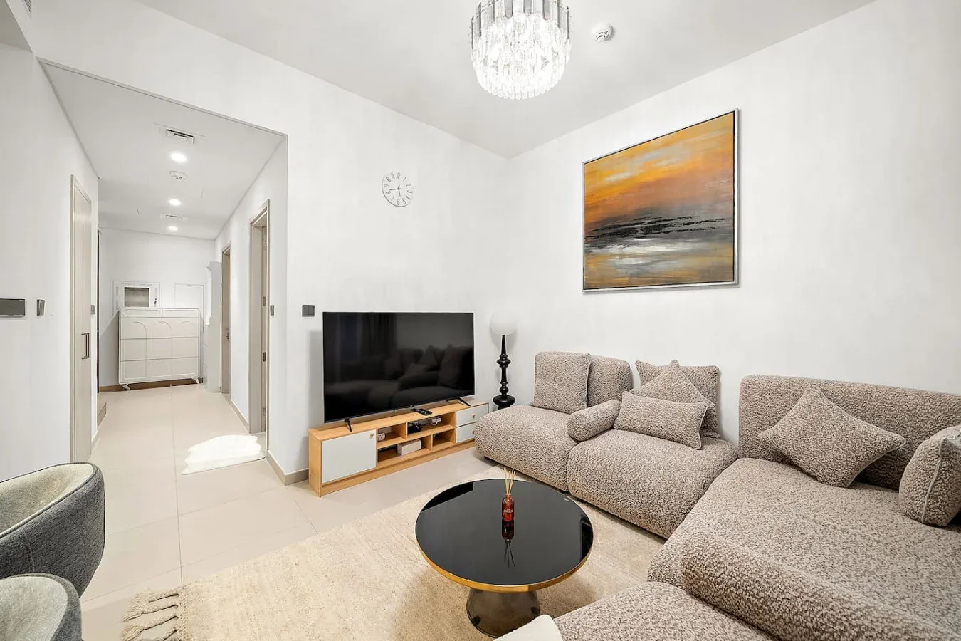 Una sala luminosa con televisor, sofá seccional y mesa de centro redonda.