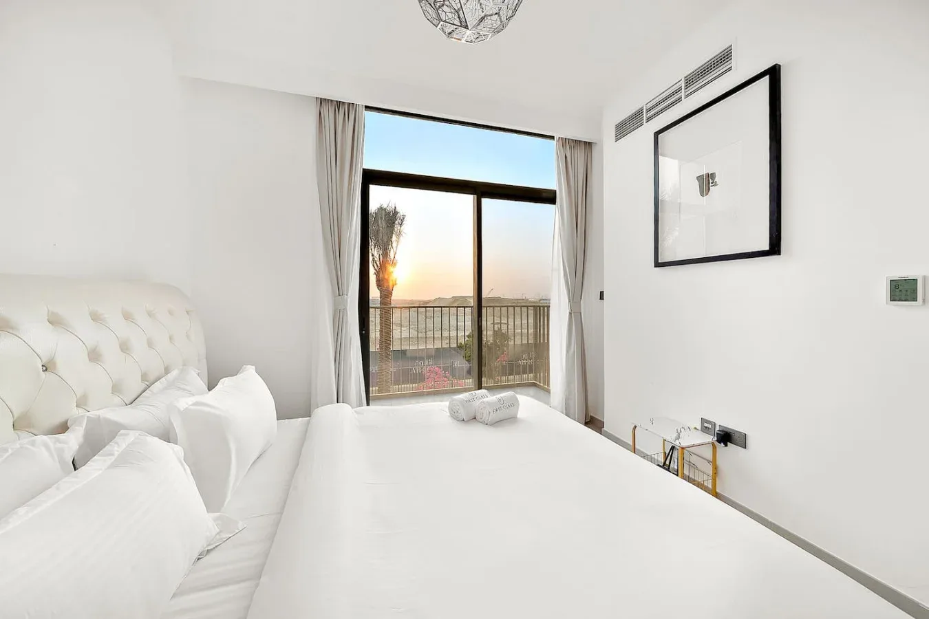 Un dormitorio luminoso con ropa de cama blanca y una gran ventana con vistas al atardecer.