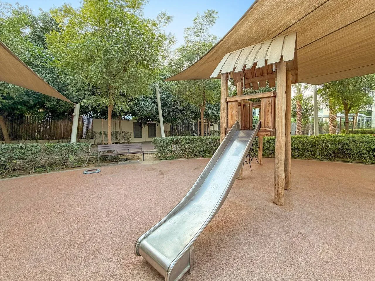 Un parque infantil sombreado cuenta con un tobogán y árboles alrededor.