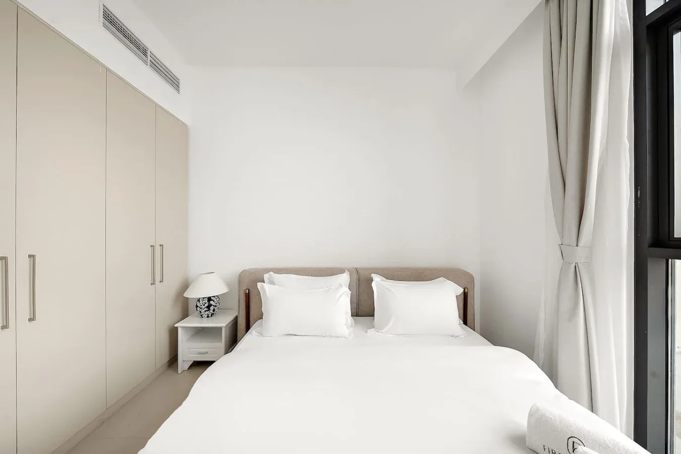 Un dormitorio luminoso con una cama bien arreglada junto a armarios empotrados.