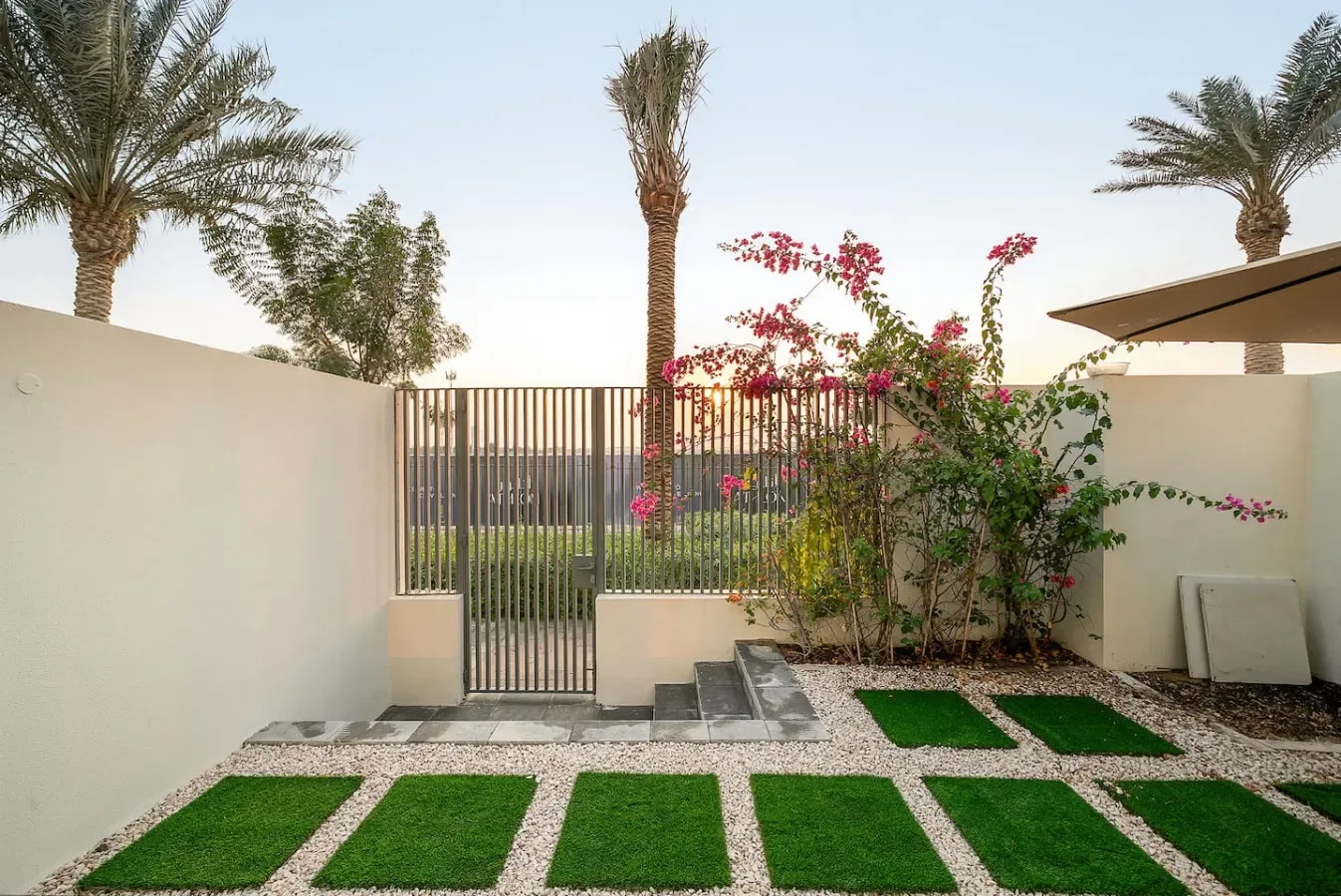 Un pequeño patio ajardinado con parches rectangulares de césped y una puerta metálica.
