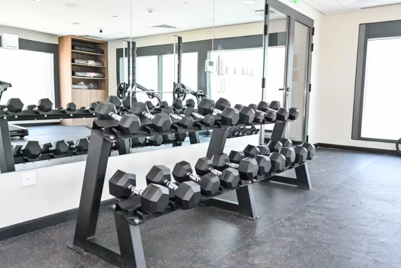 Un gimnasio luminoso con filas de mancuernas junto a paredes con espejos.