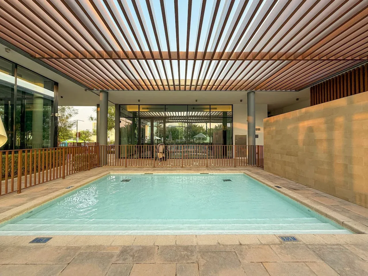 Una piscina bajo un techo de listones, con puertas de vidrio al fondo.