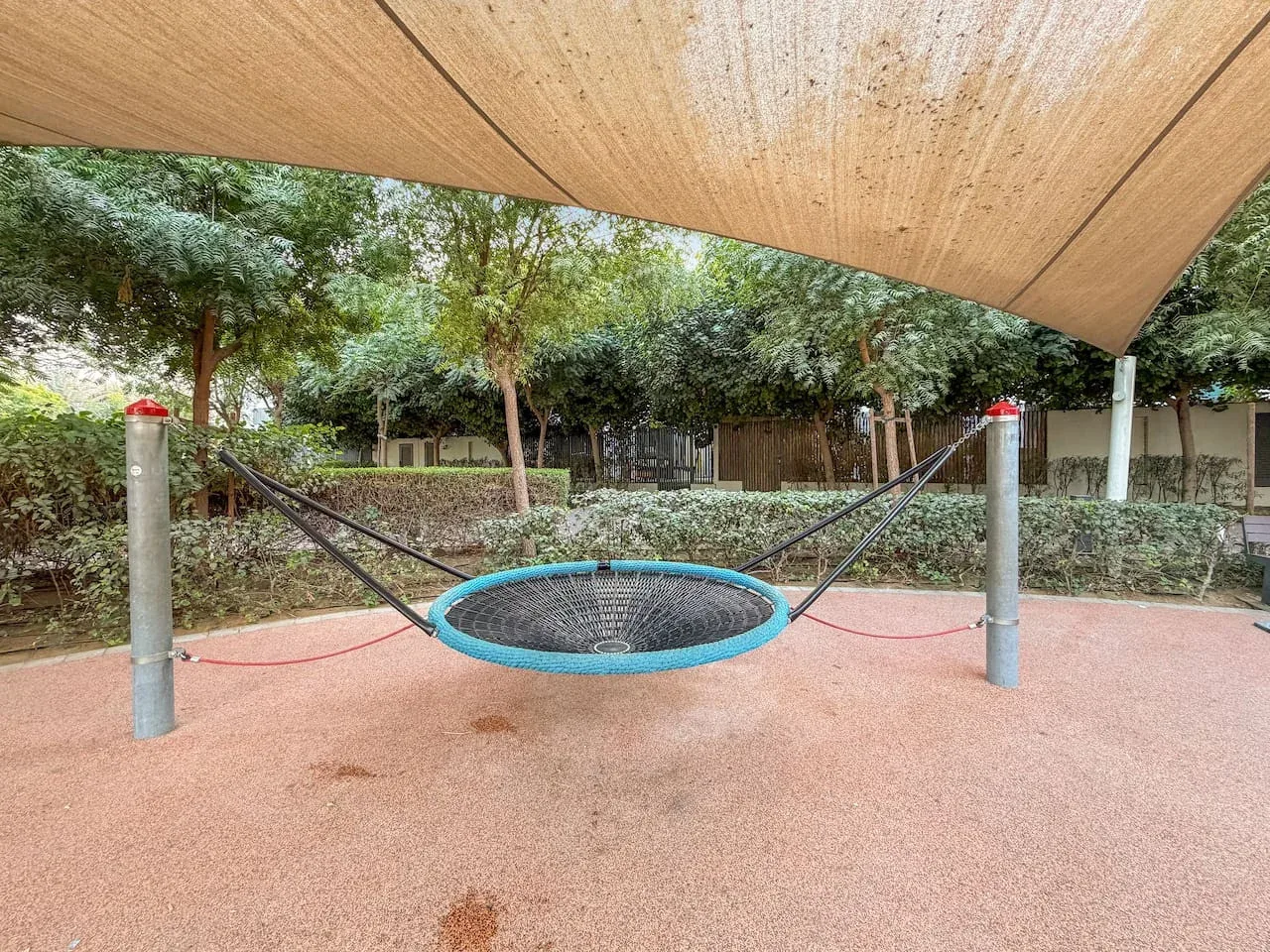 Una zona de juegos al aire libre tiene una red circular suspendida bajo una cubierta de sombra.