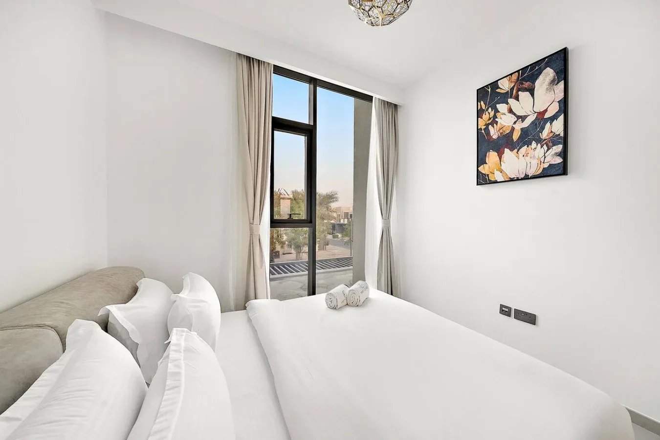 Un dormitorio luminoso con una cama, cortinas claras y una ventana grande.