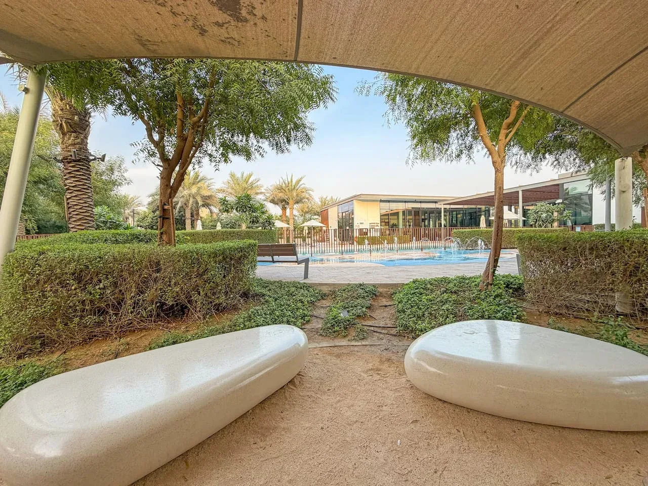 Zona de piscina exterior ajardinada con asientos bajo un toldo.