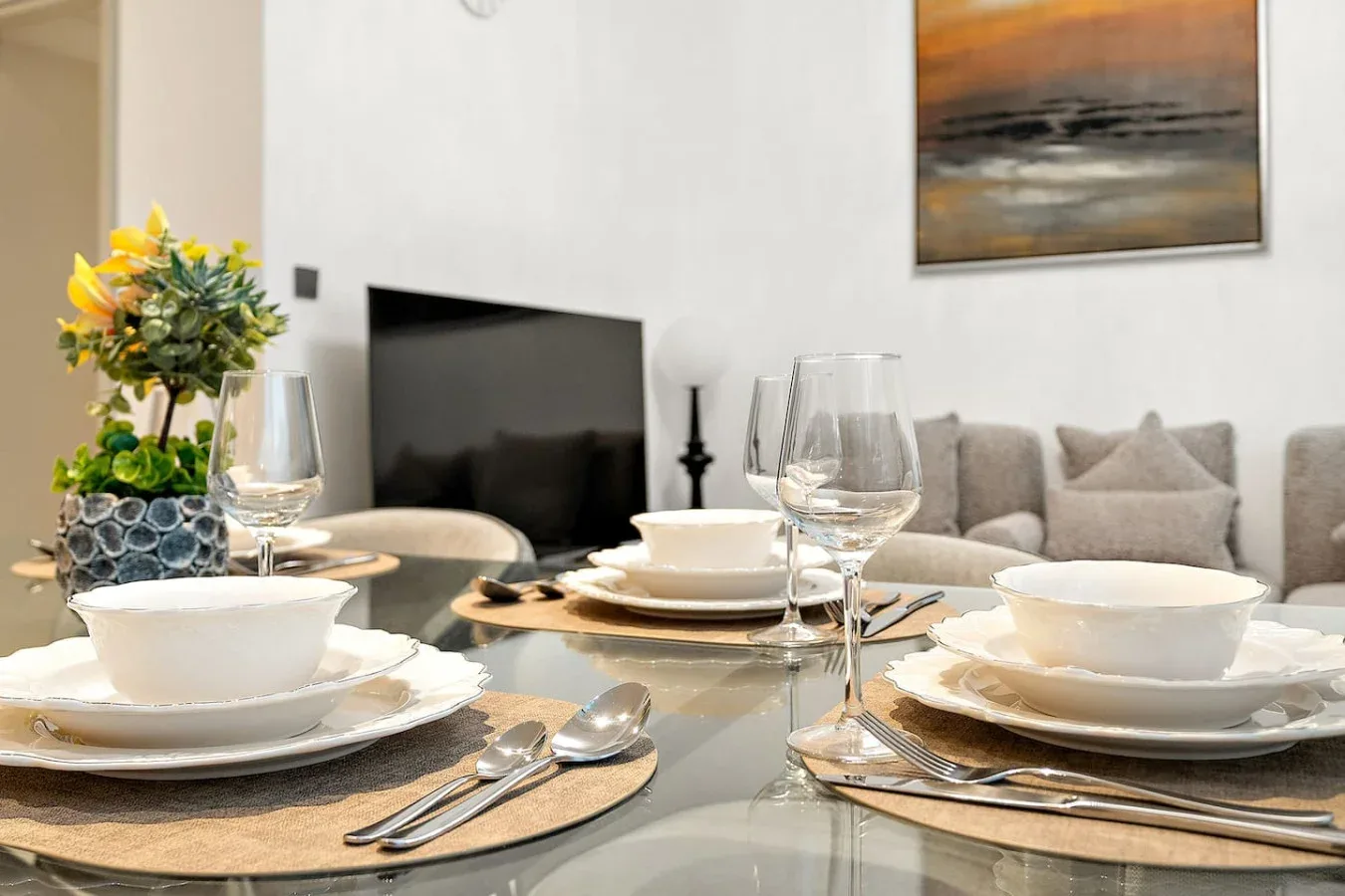 Una mesa de comedor con platos y copas está frente a una sala de estar.