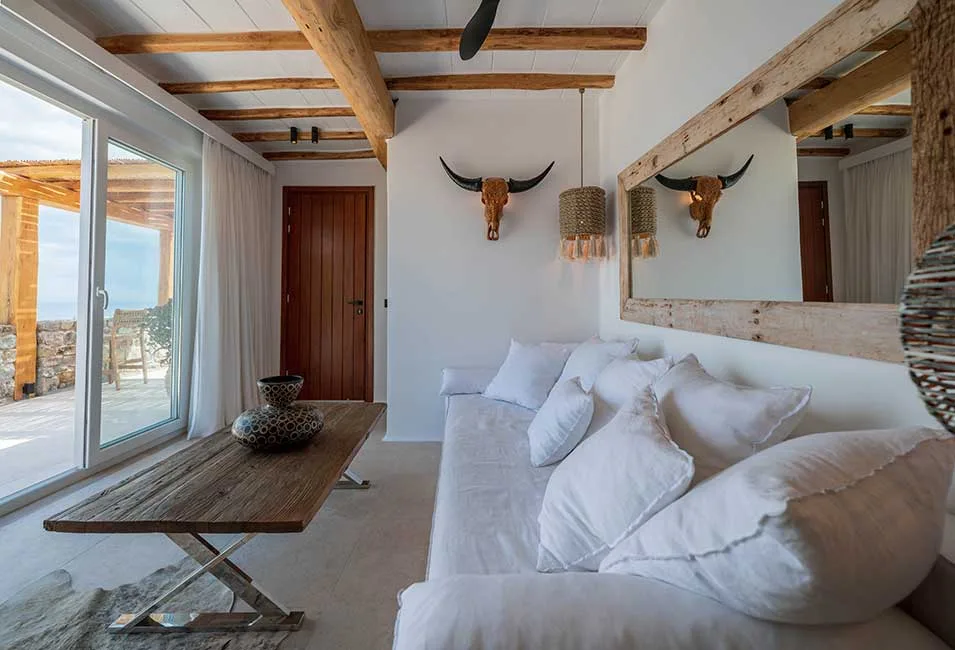 A bright living room with white seating and a wooden coffee table beside glass doors.