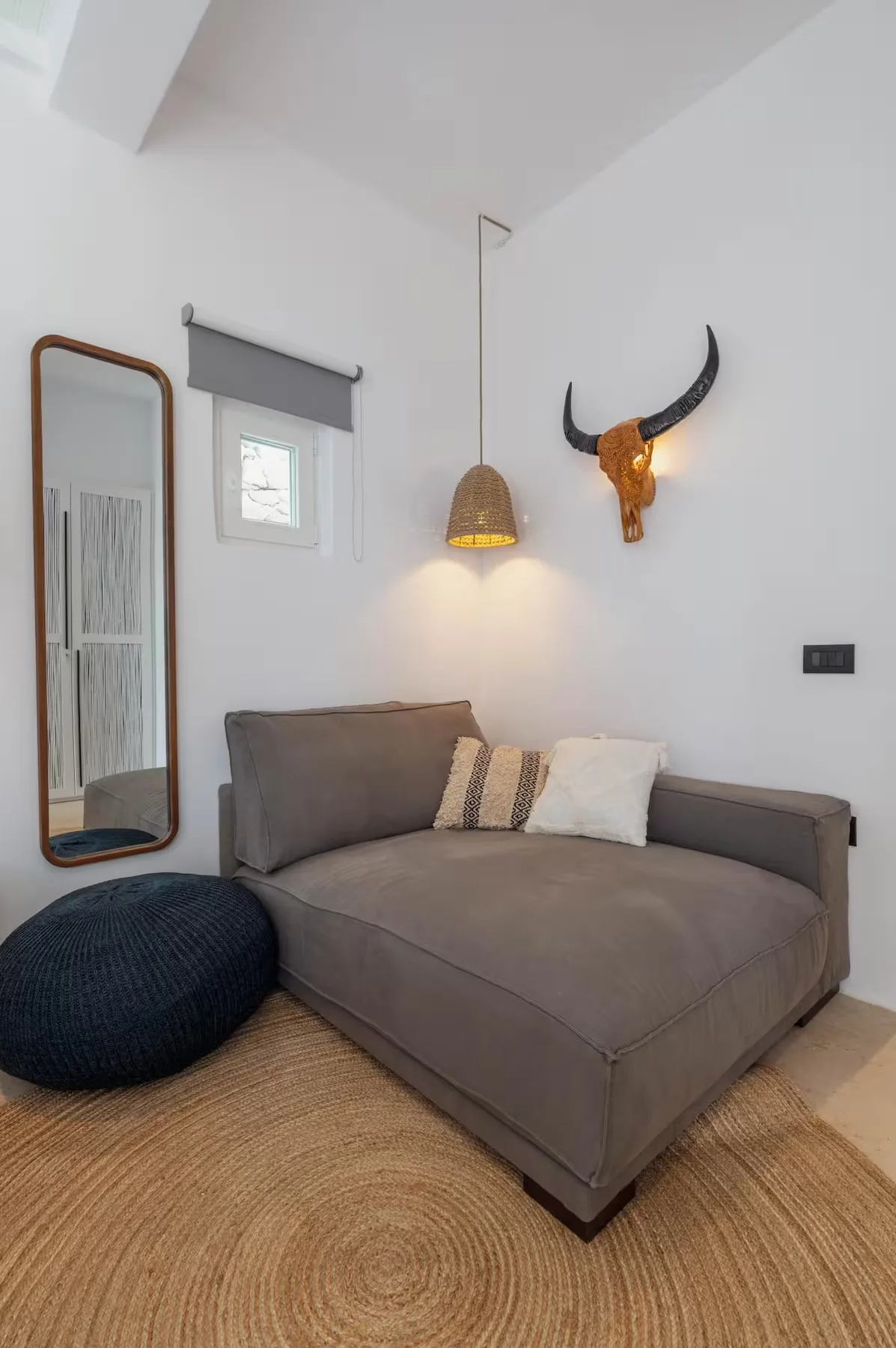 A sitting area with a gray chaise lounge, woven rug, and wall mirror.