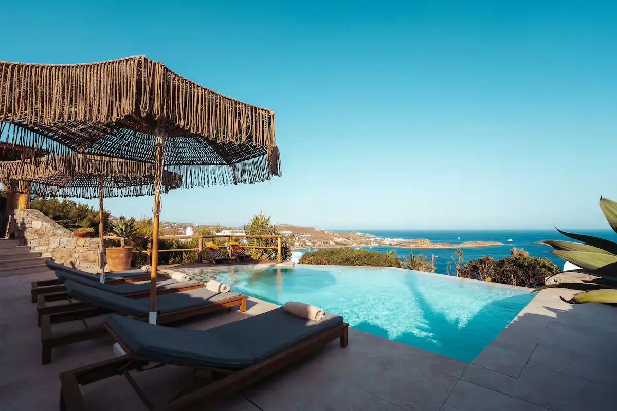 An outdoor pool terrace overlooks the sea, with shaded seating beside the water.