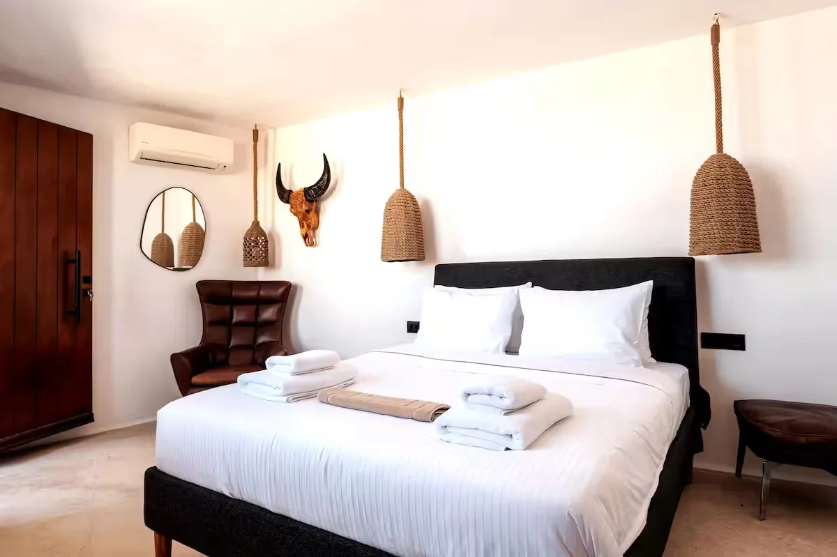 A bright bedroom with a neatly made bed and dark headboard.