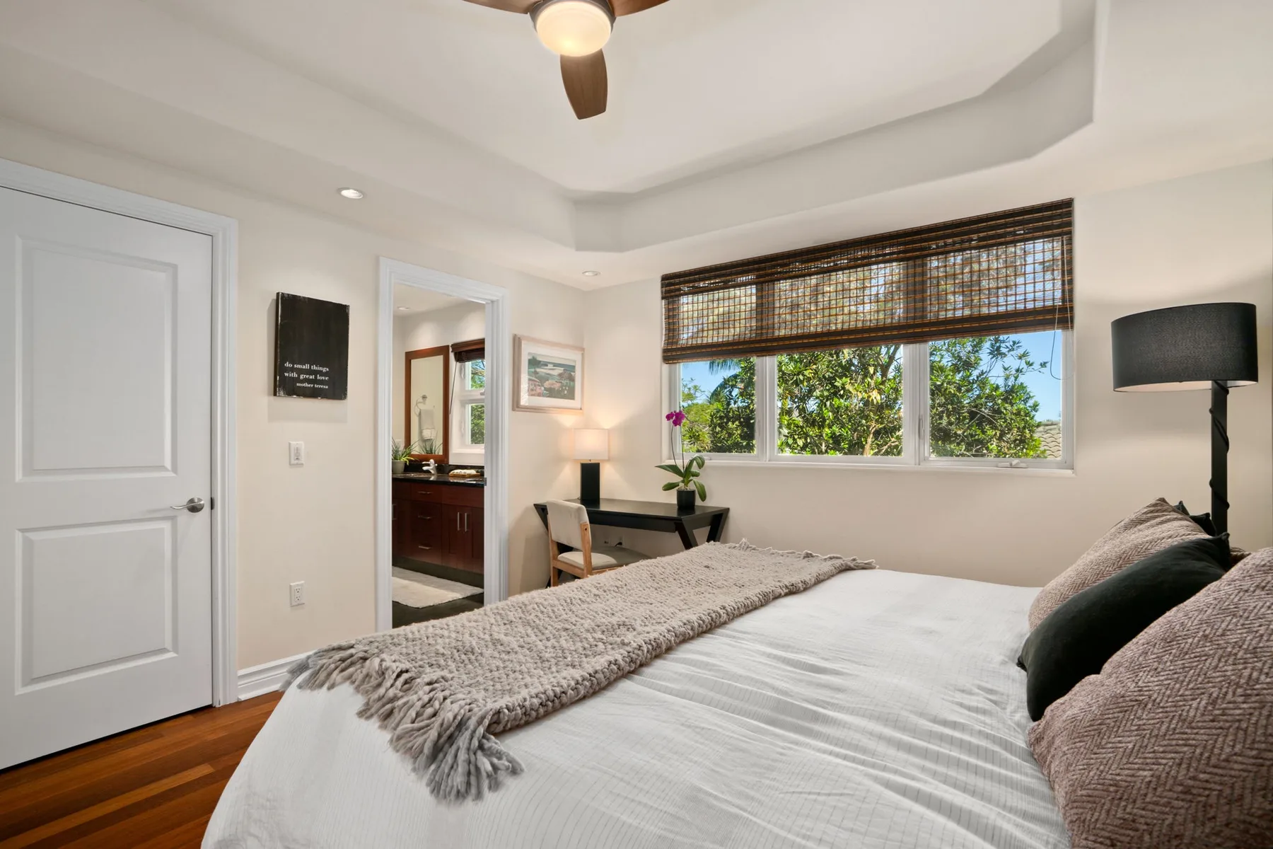 A bedroom with a neatly made bed and windows overlooking leafy greenery.