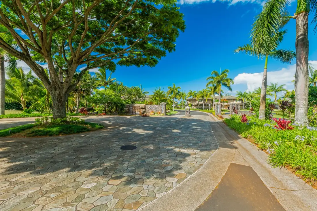 A paved outdoor driveway curves past trees and tropical landscaping.
