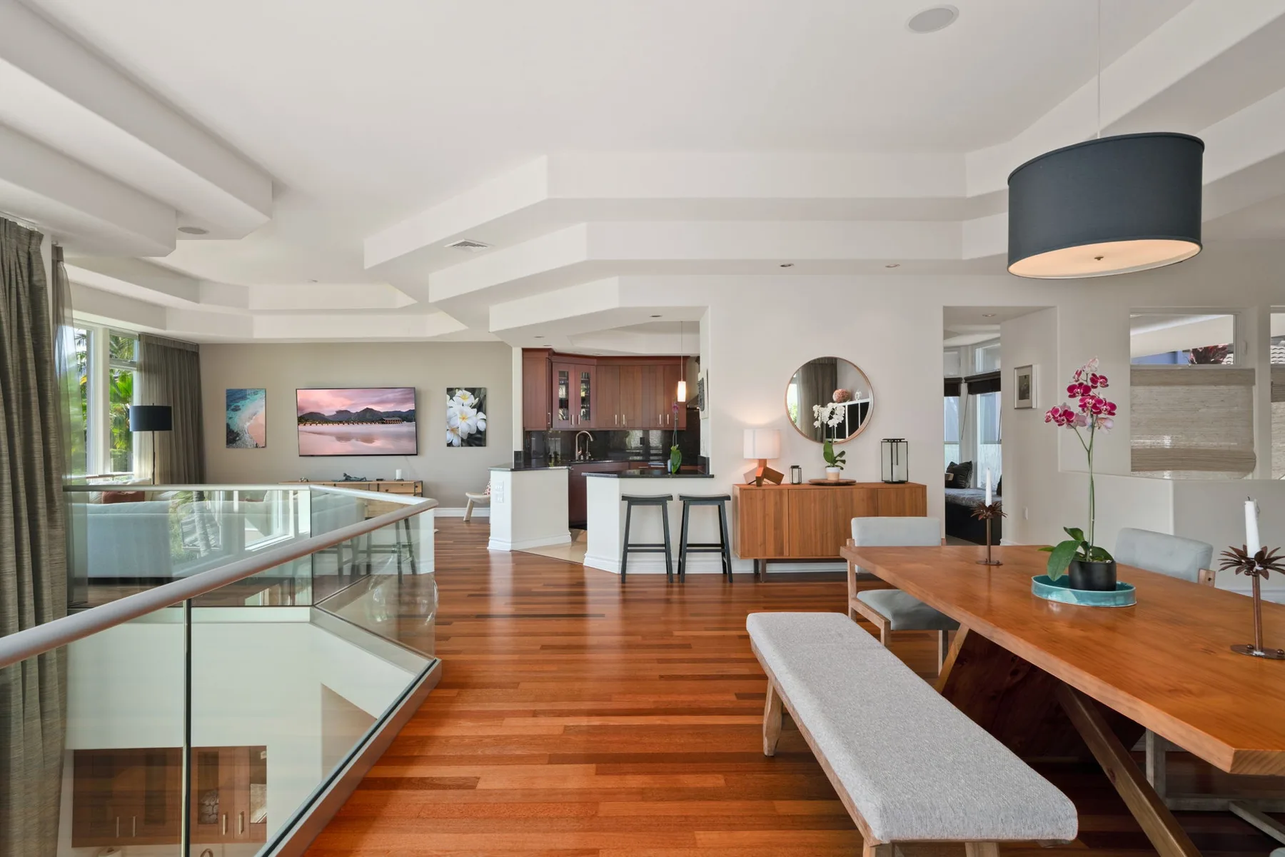 An open-plan living and dining area with a long wooden table and glass railing.
