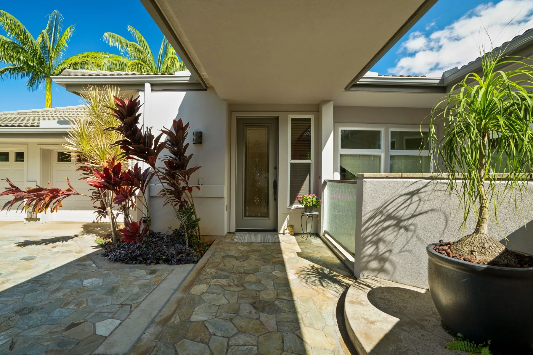 A tiled courtyard entrance with tropical plants and a shaded walkway.