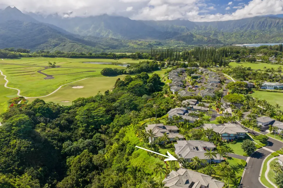 An aerial view of a landscaped resort beside green fields, with mountains in the distance.