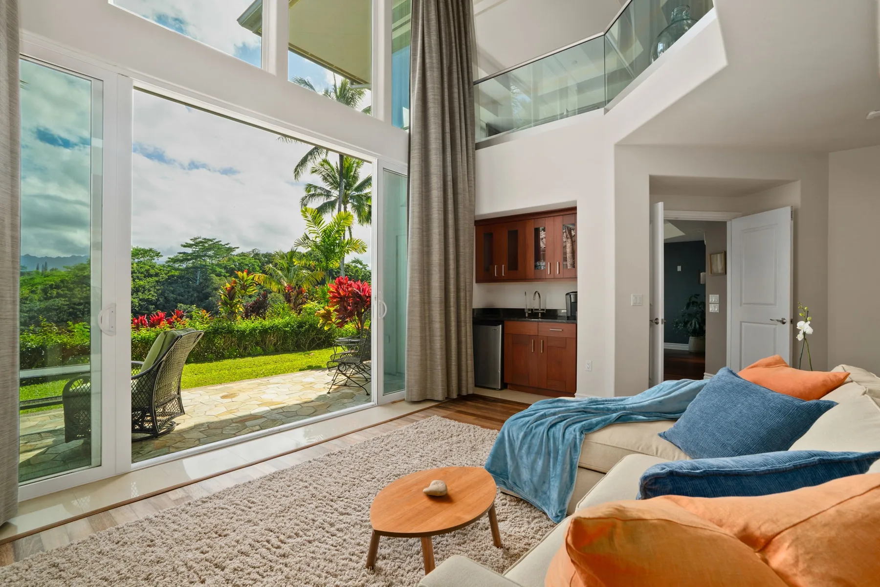 A bright living room opens onto a garden through floor-to-ceiling windows.