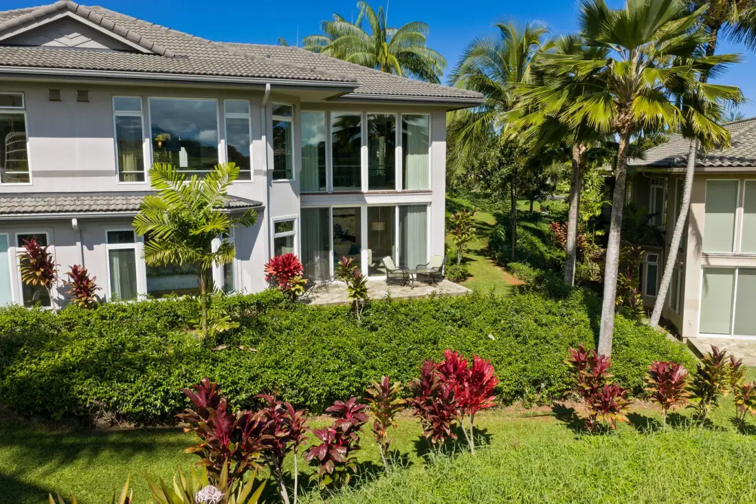 A large house stands behind a landscaped lawn with palms and shrubs.