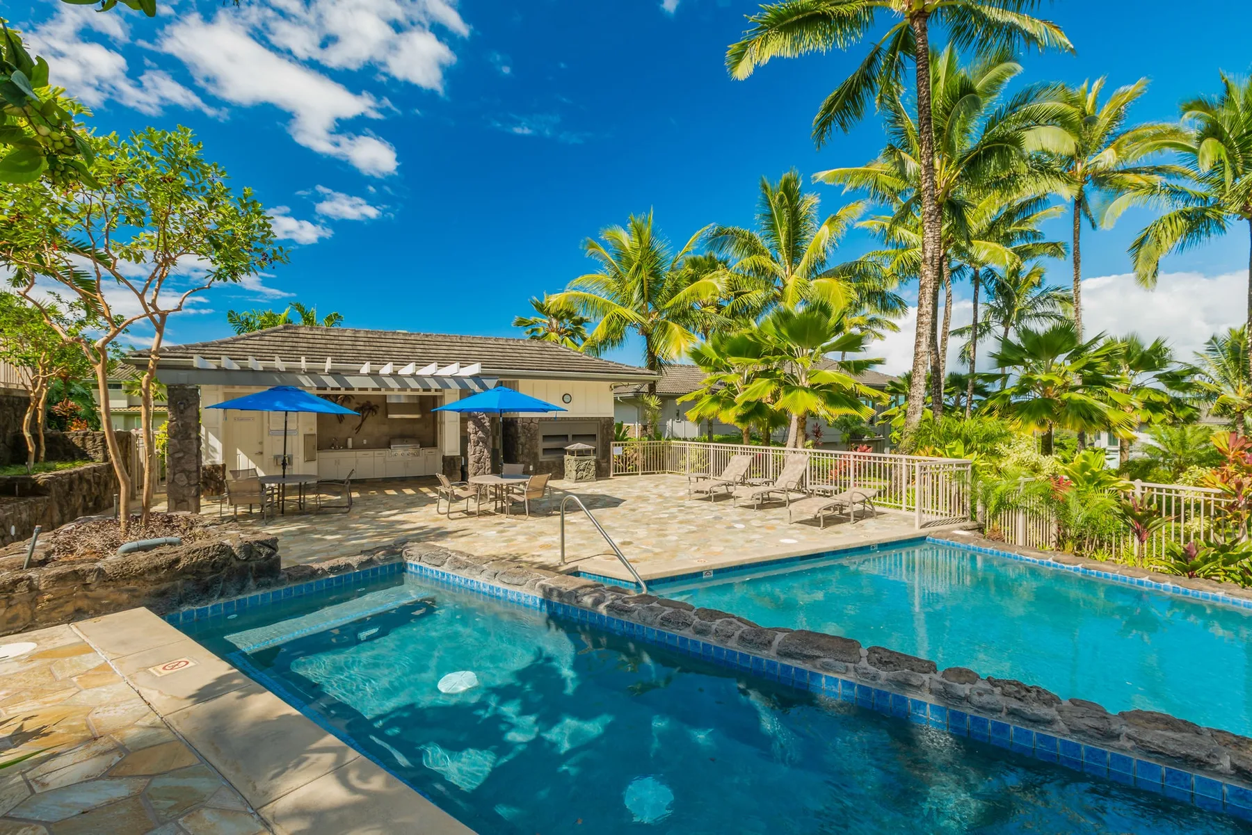 An outdoor swimming pool sits beside a tiled patio with shaded seating.