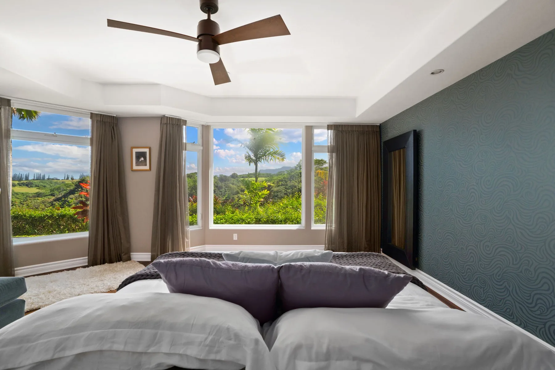 A bedroom with a bed facing broad windows overlooking green hills.