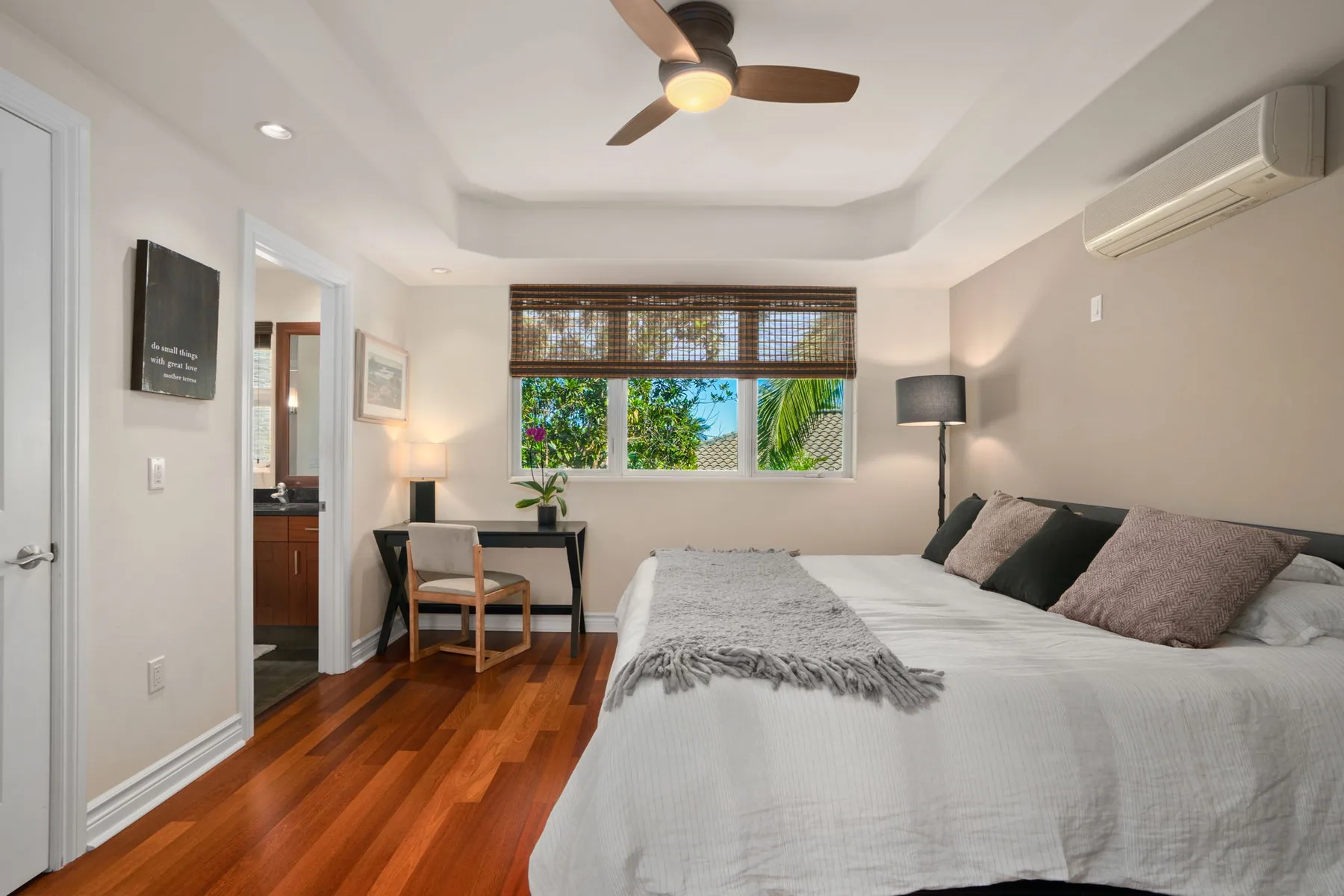 A bright bedroom with a large bed, a desk, and a window overlooking greenery.