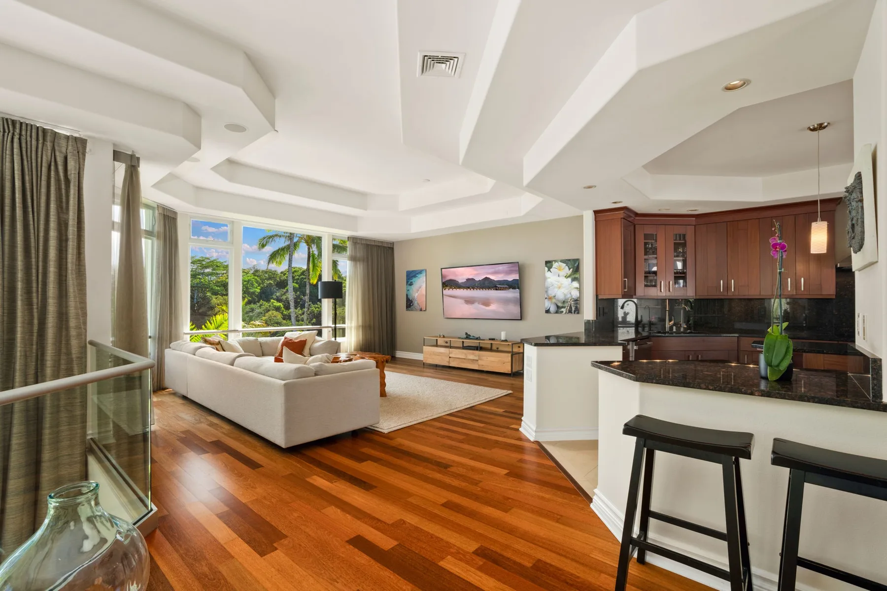 A bright open-plan living room and kitchen with large windows and wood flooring.
