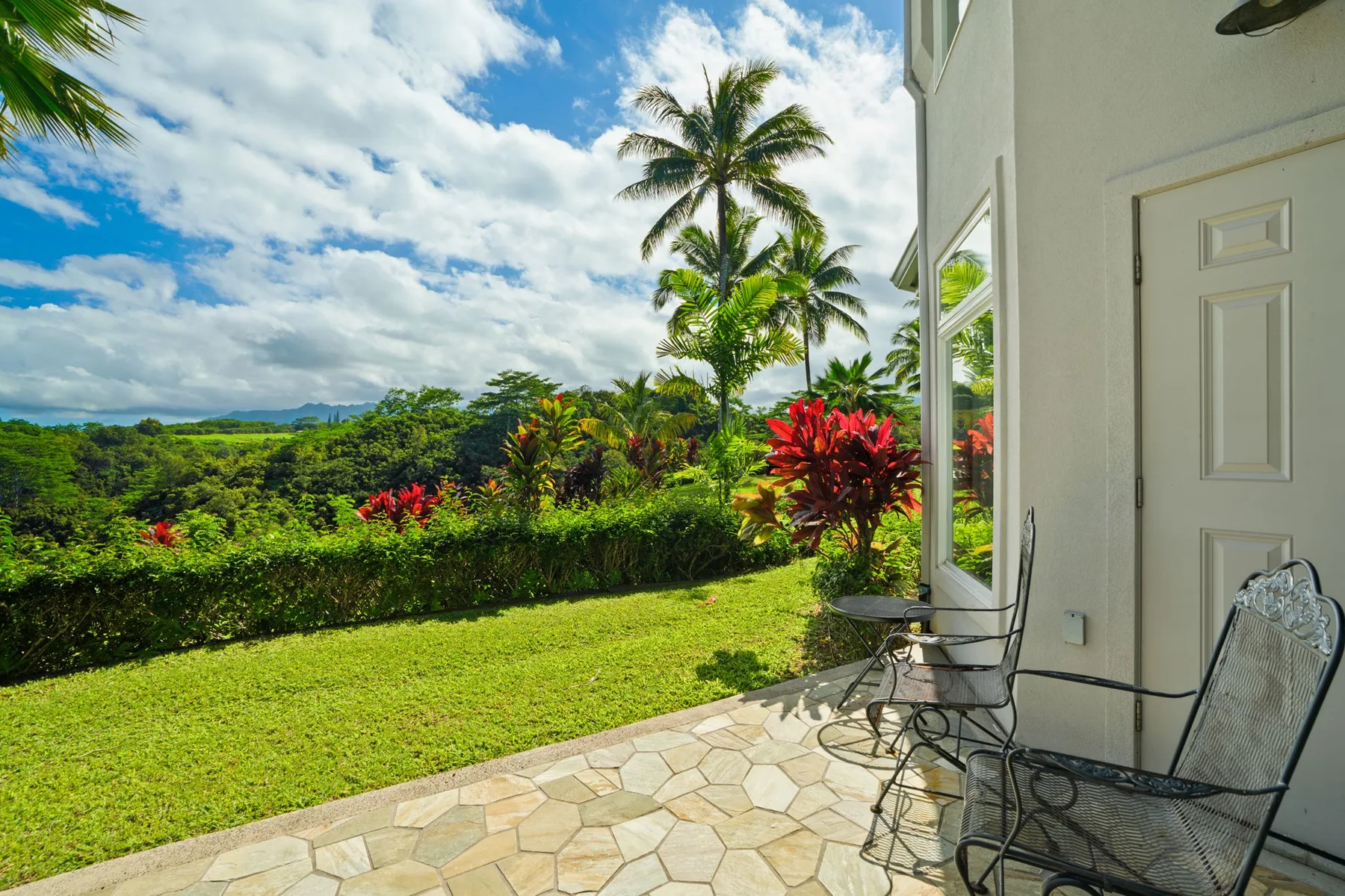 A tiled patio with seating overlooks a green garden and tropical landscape.