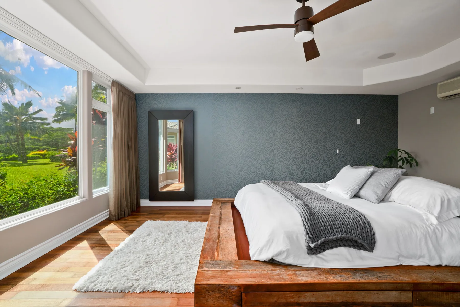 A bedroom with a bed, a large window, and a view of greenery.