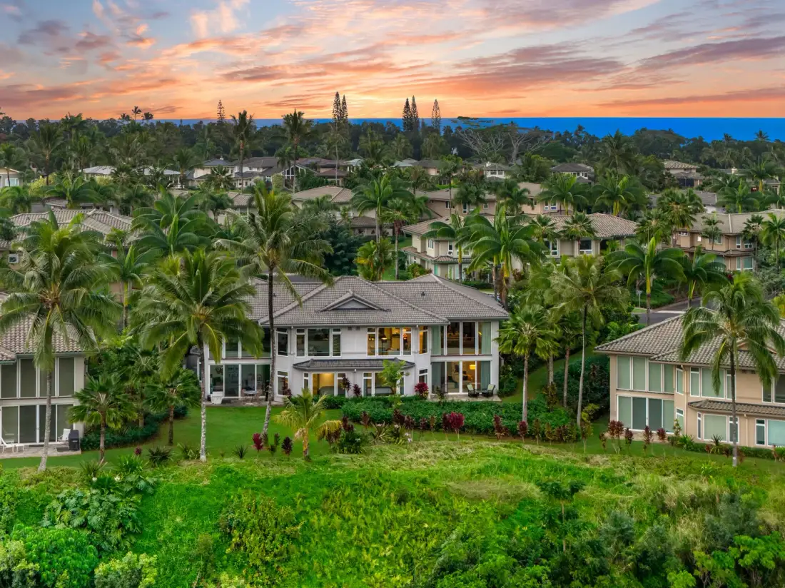 A tropical resort with low-rise buildings set among palm trees beneath a colorful sunset sky.