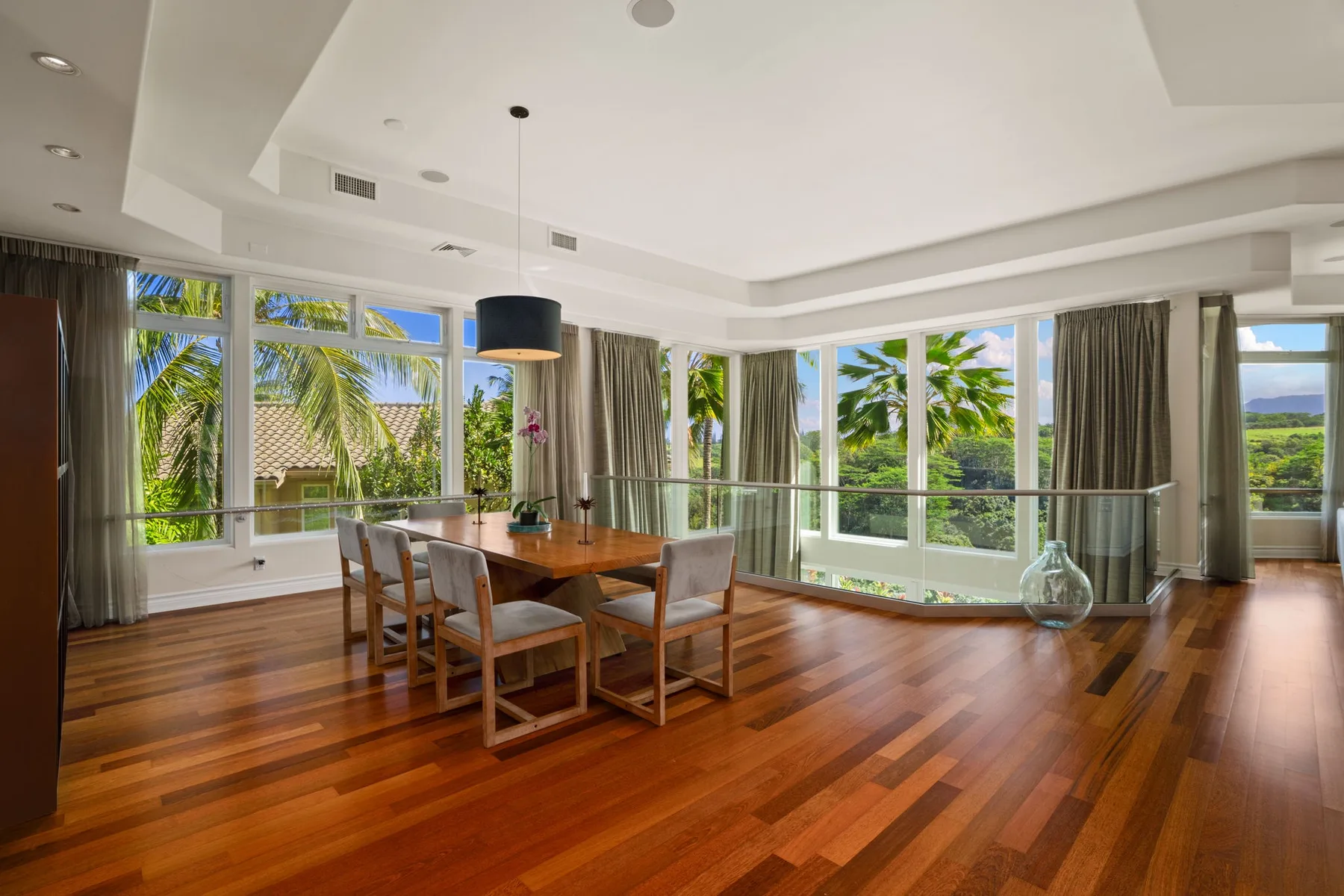 A bright dining area with a wooden table beside large windows overlooking greenery.
