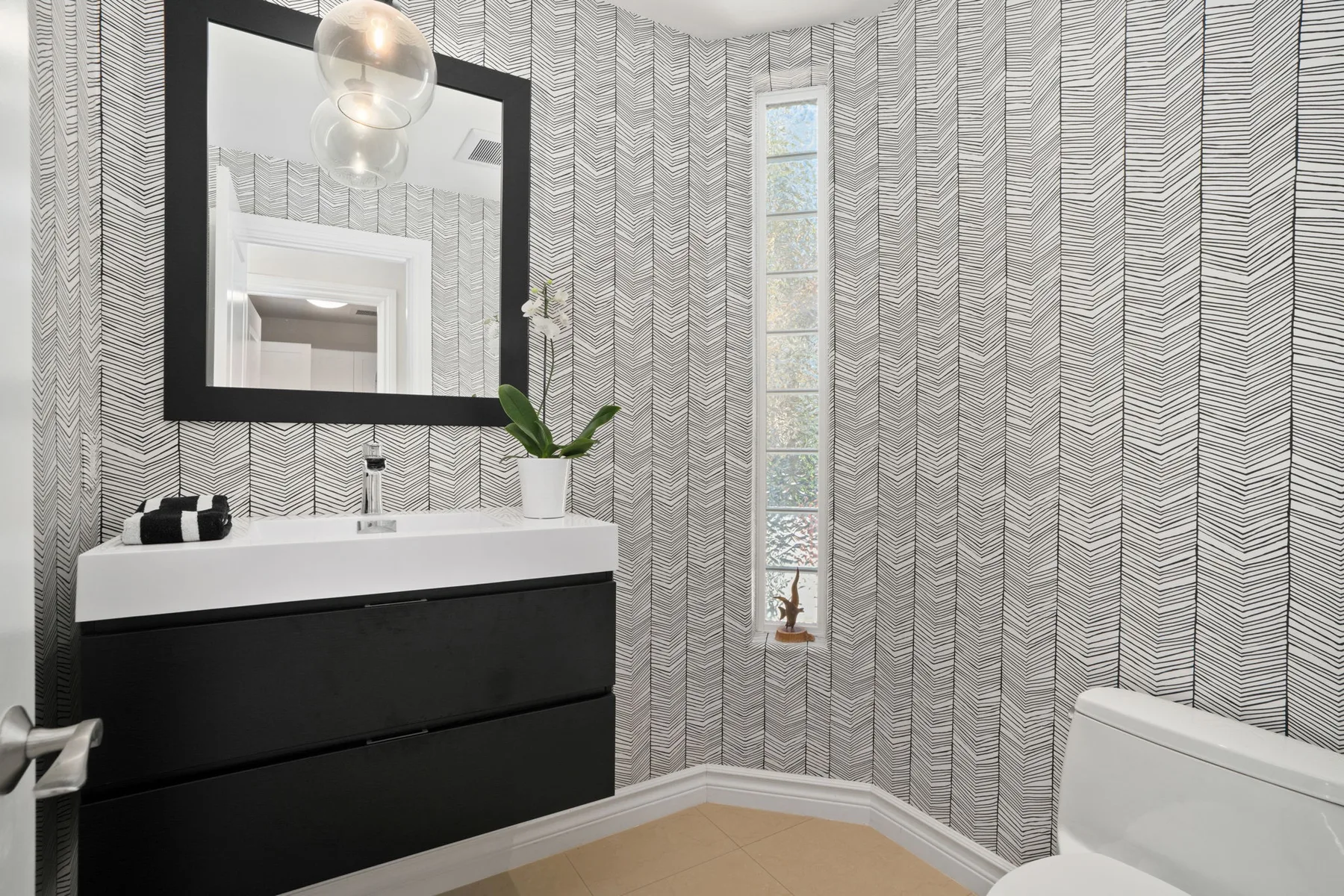 A modern bathroom features a vanity, mirror, and narrow window.