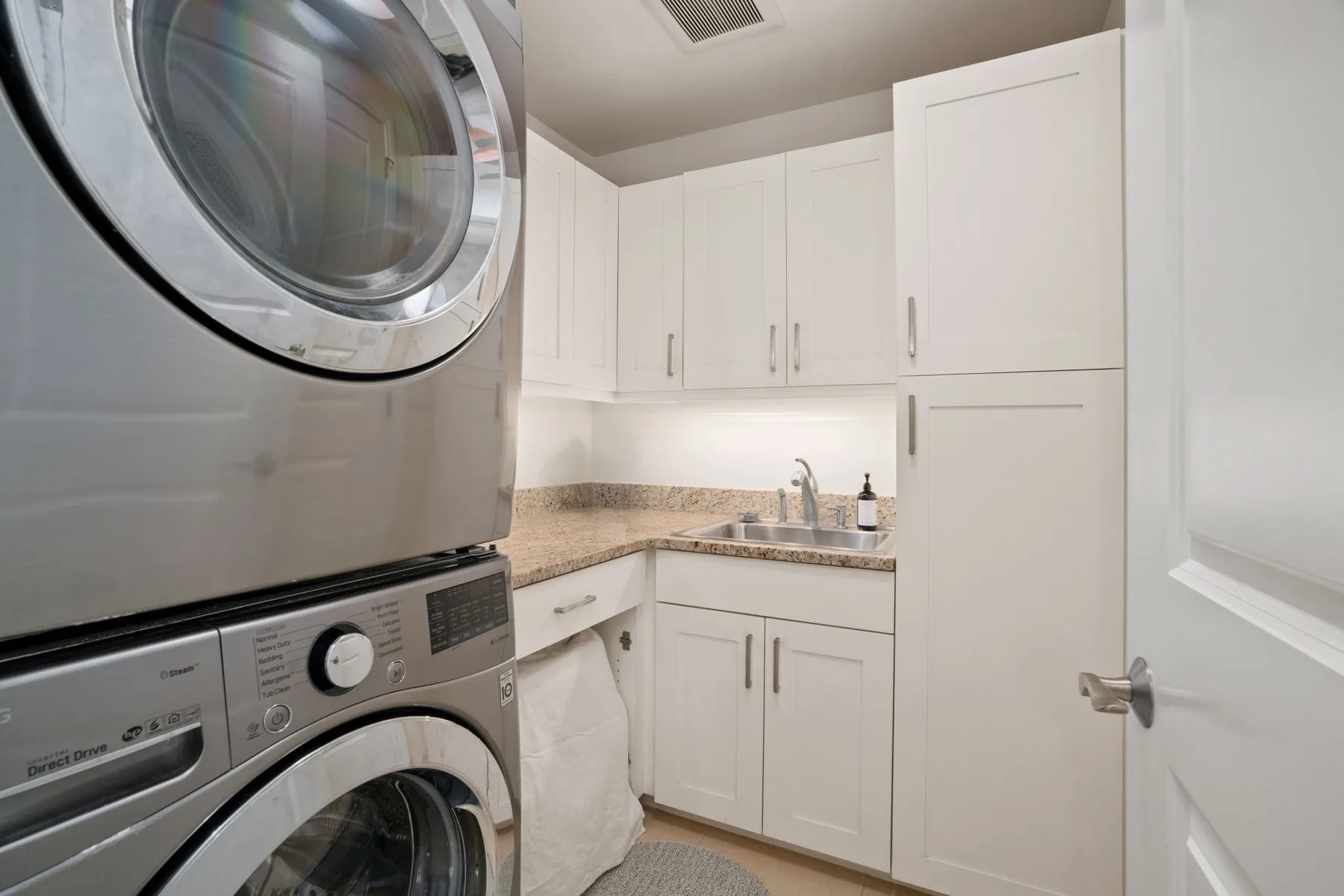 A laundry room with stacked laundry machines beside white cabinets and a sink.