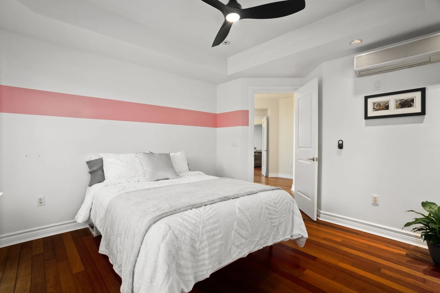 A bedroom with a bed, a pink wall stripe, and a ceiling fan.