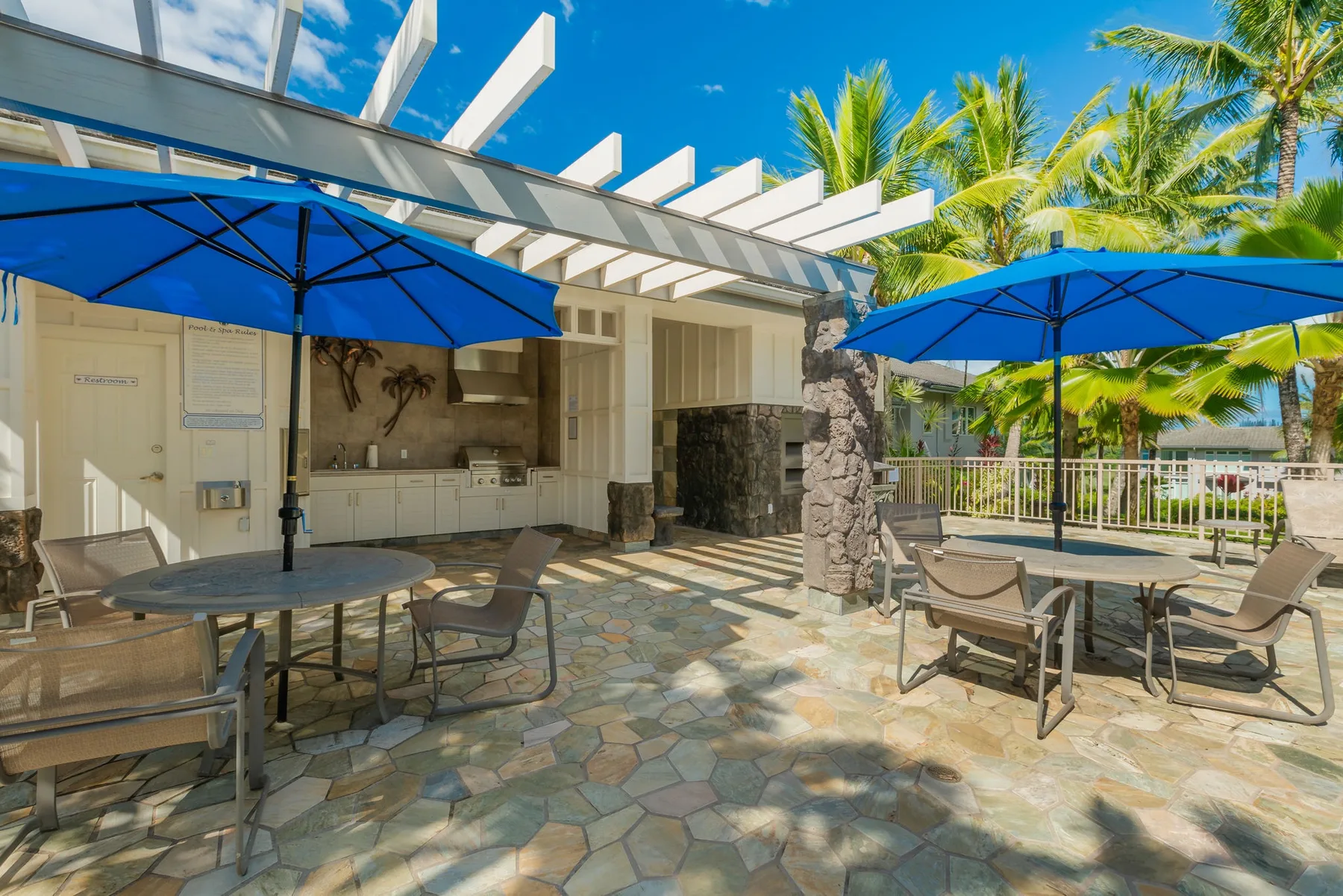 An outdoor patio with seating, blue umbrellas, and a built-in kitchen.