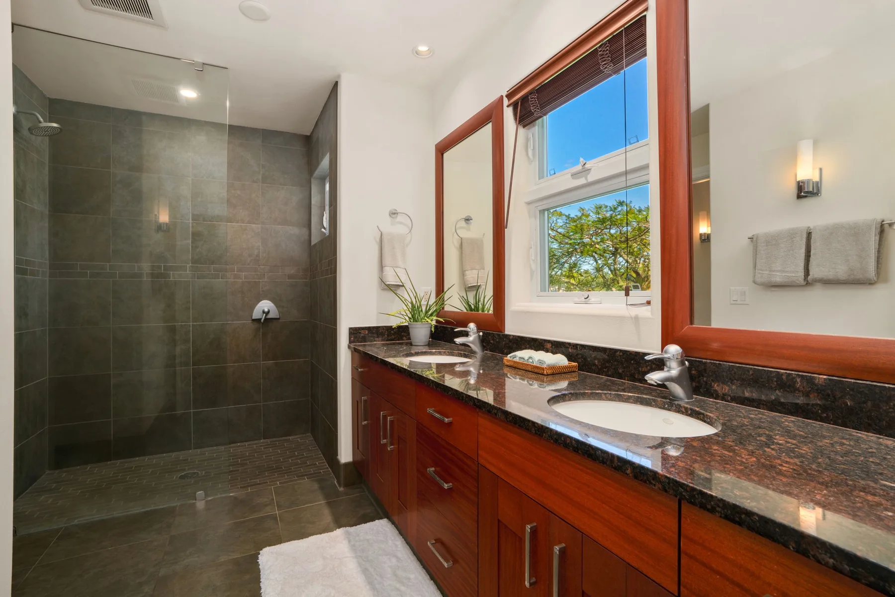 A bathroom with a glass shower, a long vanity, and a window.