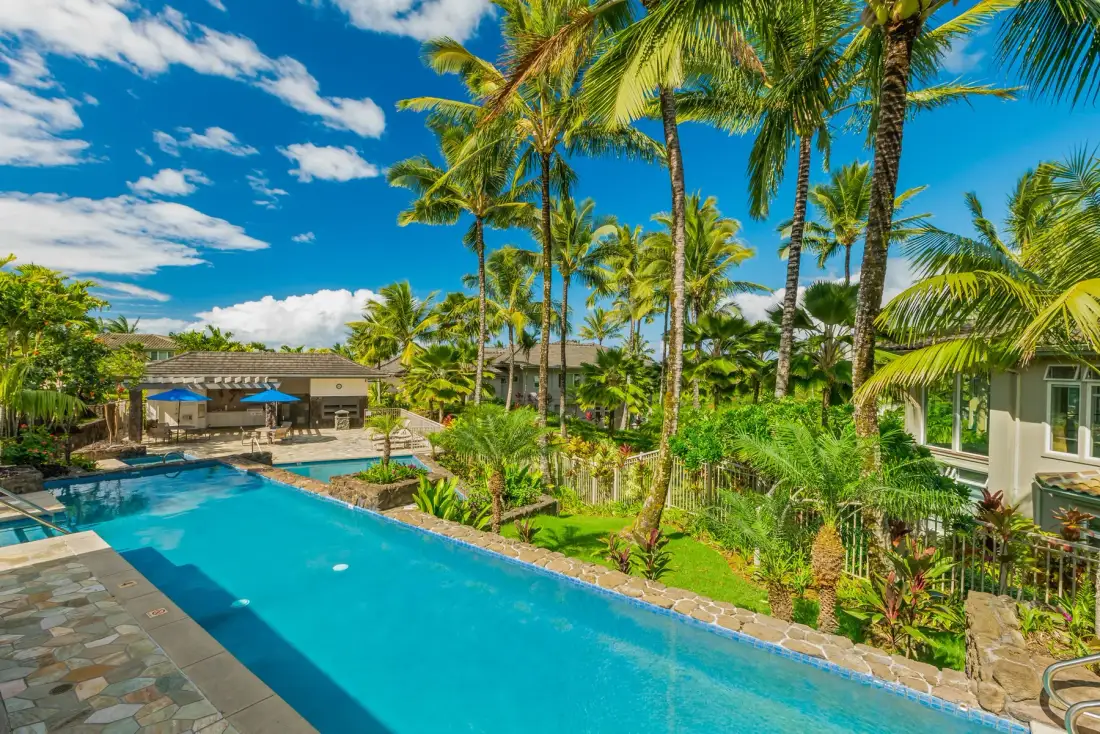 A tropical pool area surrounded by palm trees and greenery.