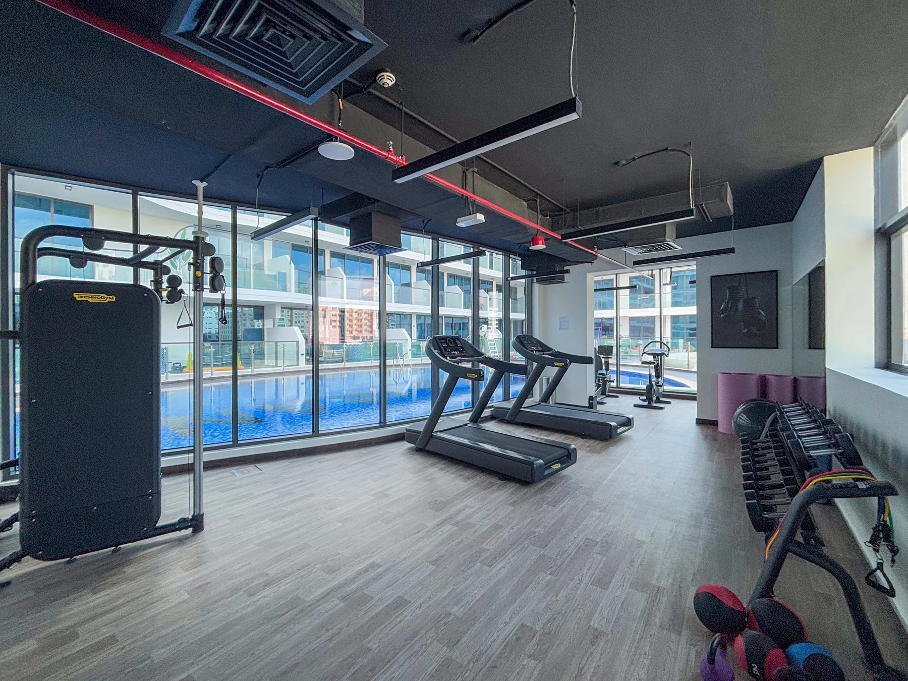A gym with treadmills and exercise equipment beside large windows.