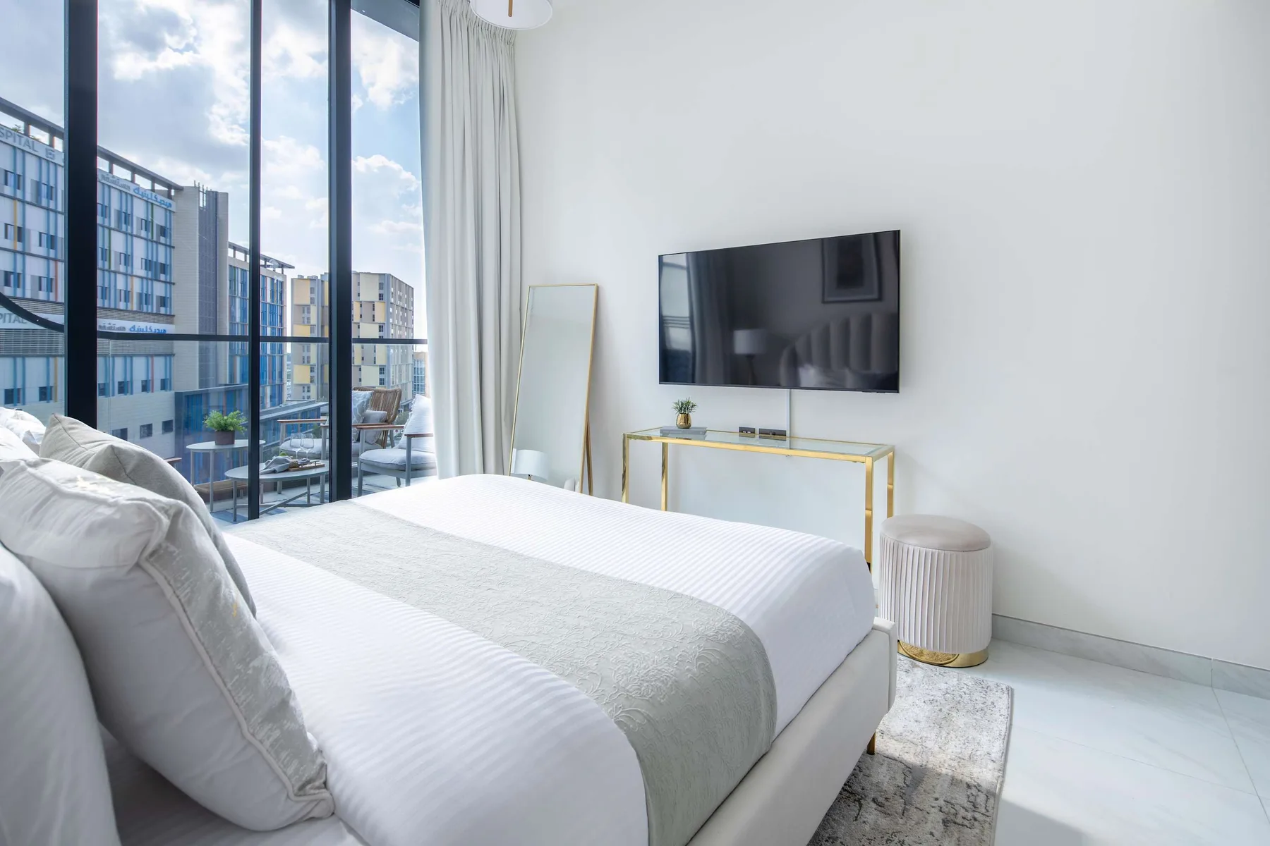 A bright bedroom with a bed beside floor-to-ceiling windows.