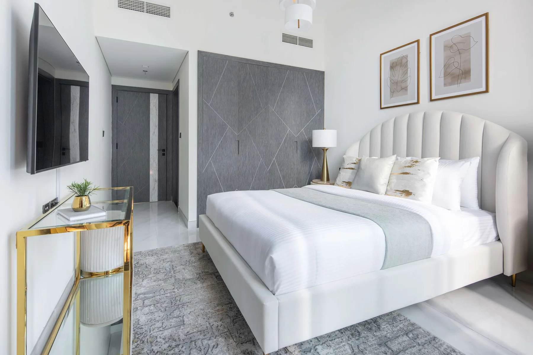A bright bedroom with a large bed, pale bedding, and framed artwork.