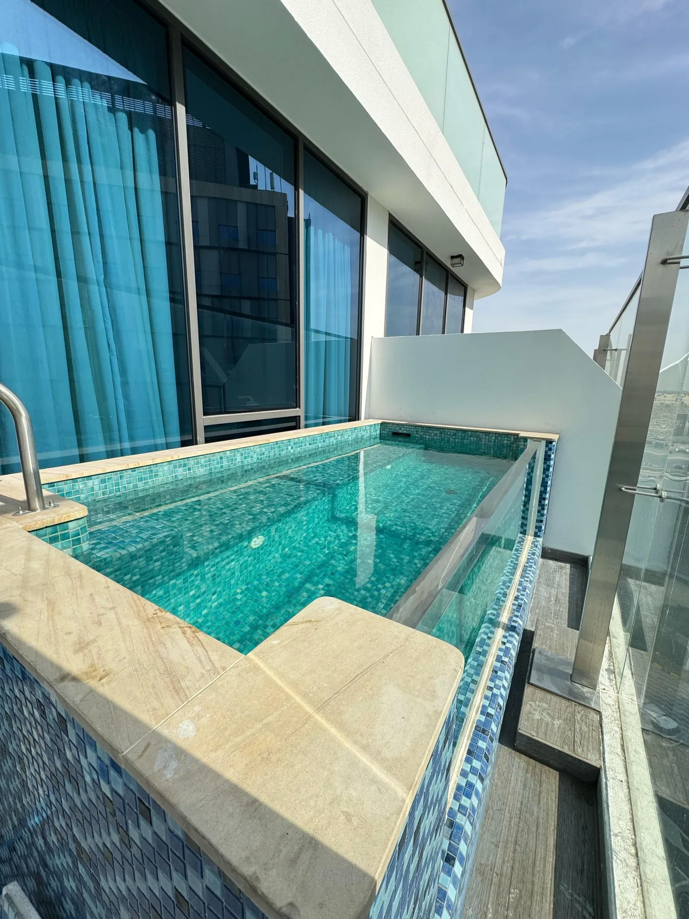 A small outdoor pool beside a modern building, with glass doors and blue water.