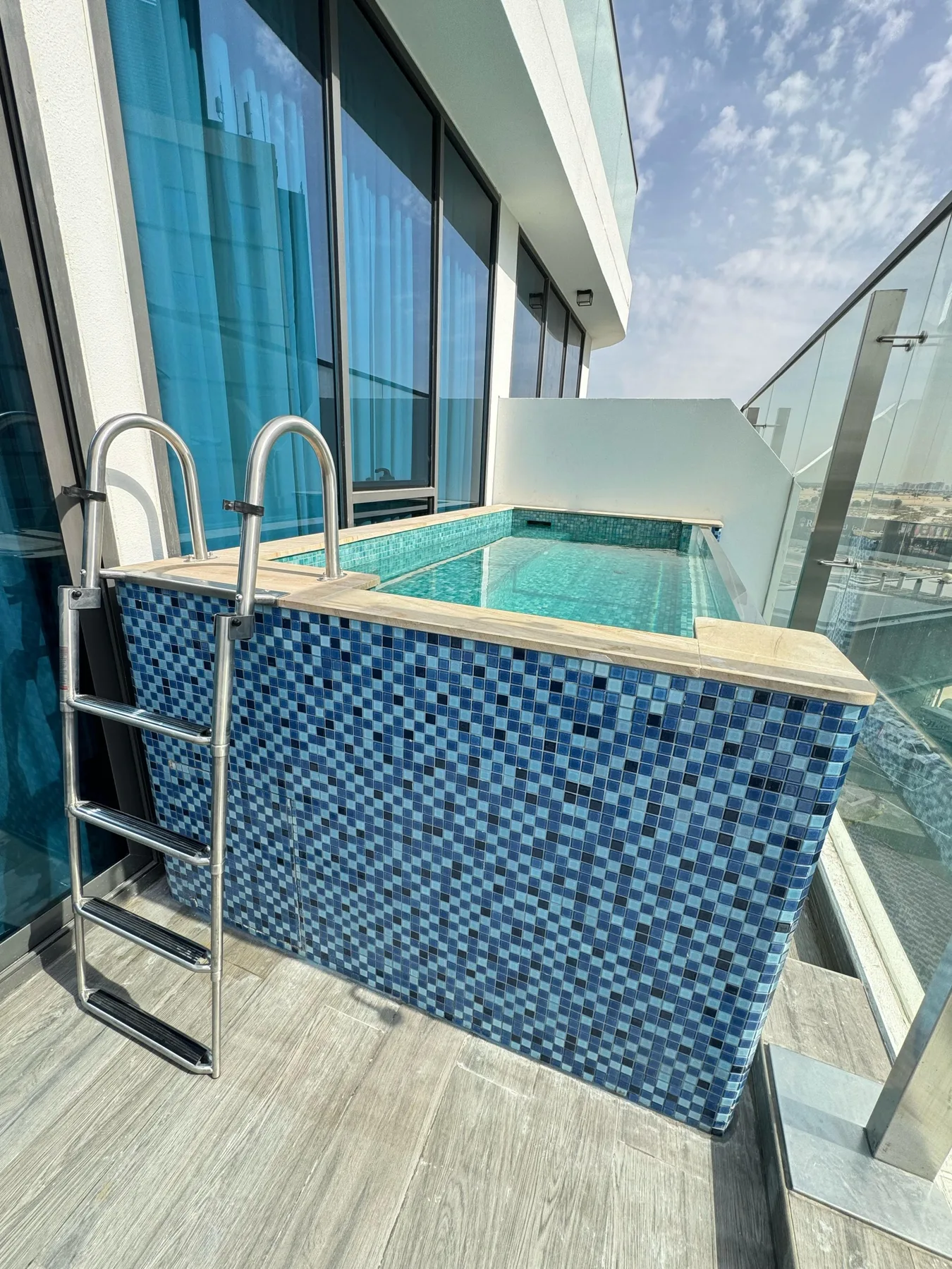 A small outdoor pool sits beside floor-to-ceiling windows and a glass railing.