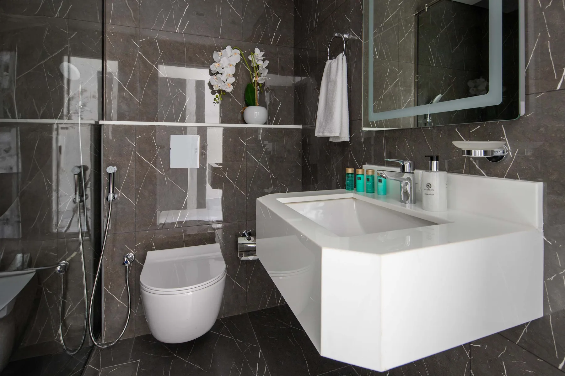 A modern bathroom with a wall-mounted sink, toilet, and dark tiled walls.